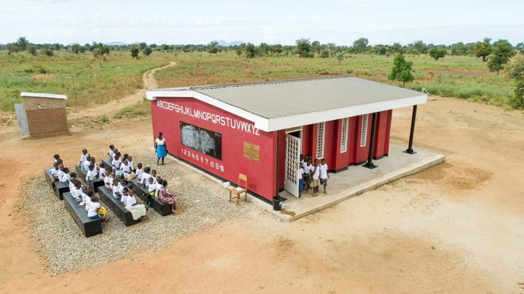 Students sitting outside a 3D printed school in Malawi