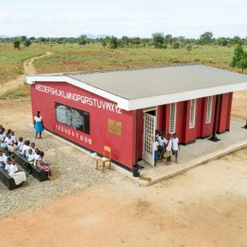 Students sitting outside a 3D printed school in Malawi