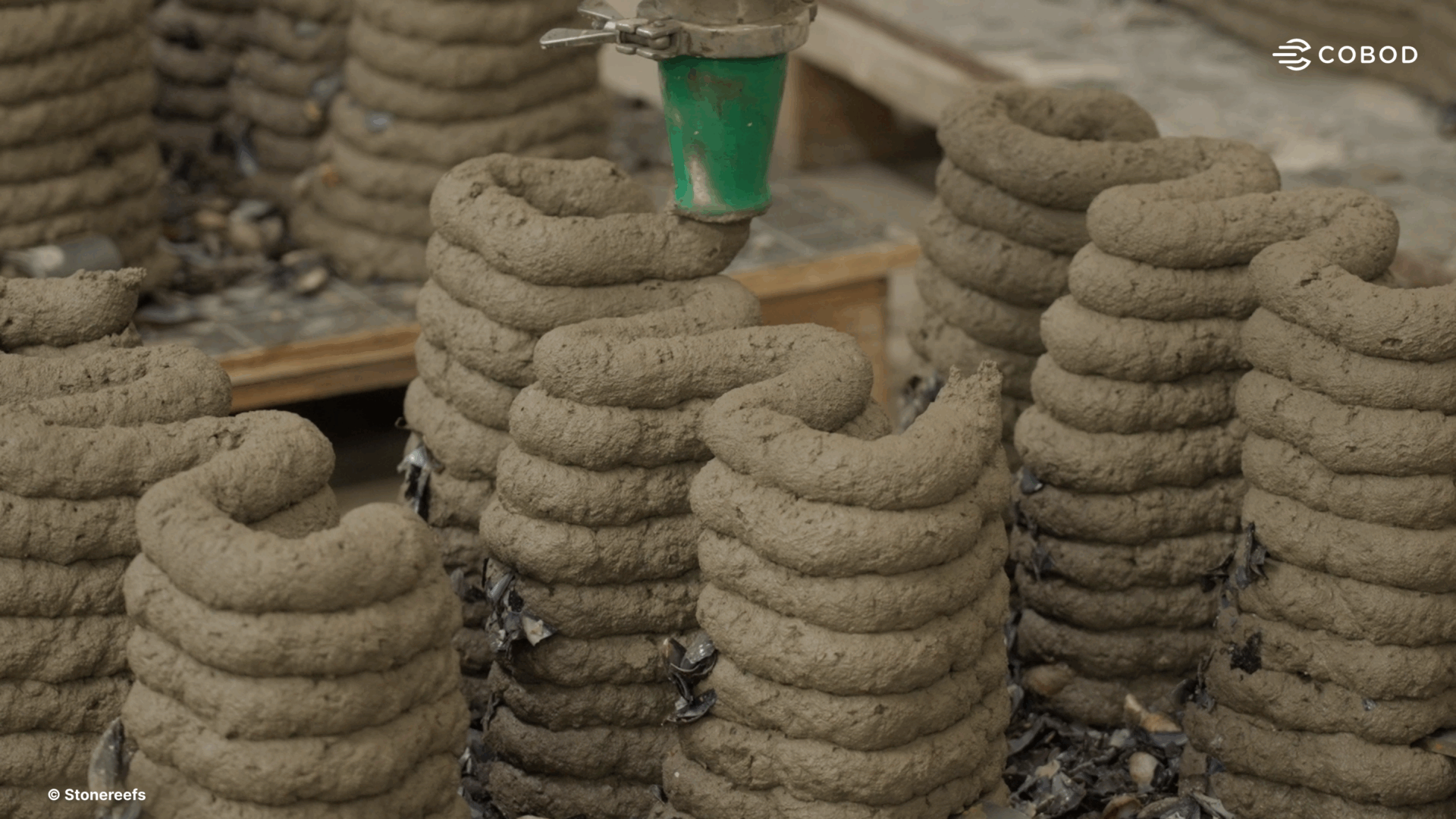 Close-up of a 3D printer nozzle extruding layered concrete in coiled shapes to create artificial reef structures for marine habitats.