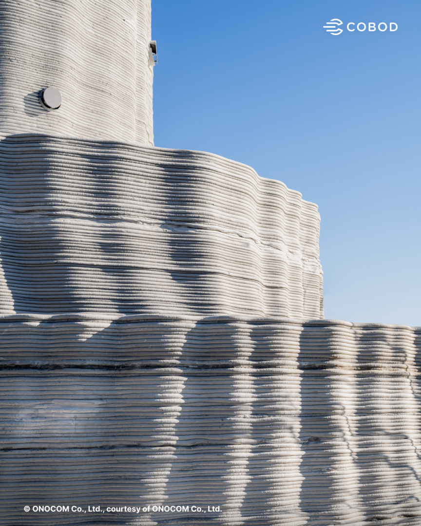 Daytime close-up exterior view of Japan’s first government approved two-story 3D printed reinforced concrete house, showing the layered concrete walls and curved geometry produced through on-site 3D construction printing.