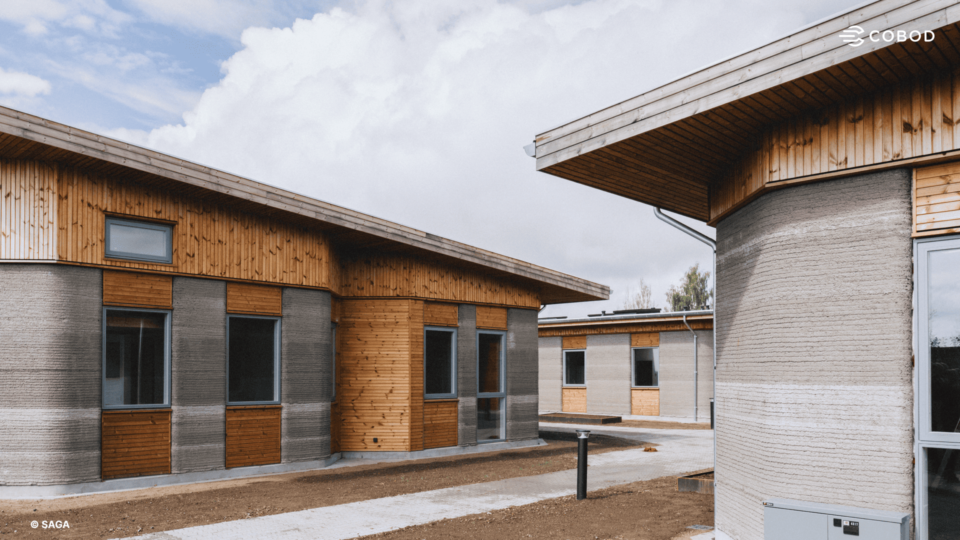 Exterior of two building clusters, showing 3D-printed concrete walls with timber cladding and sloping roofs.